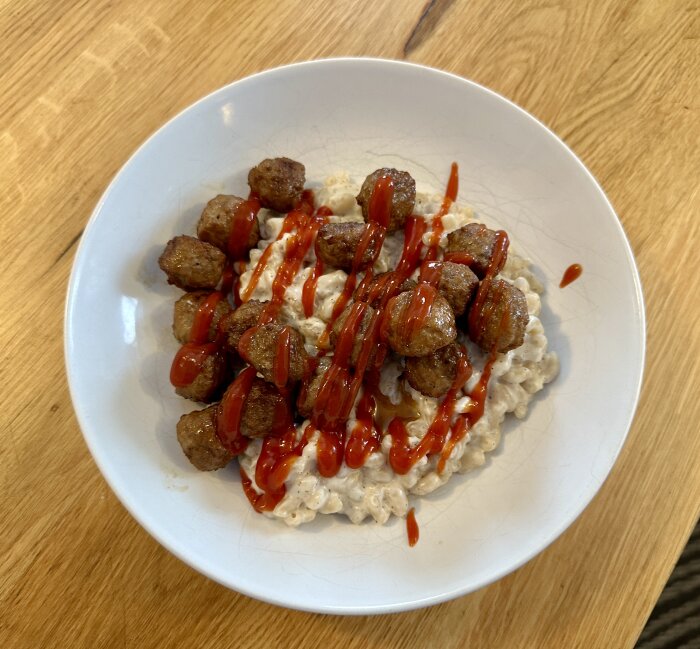 Köttbullar med ketchup på en tallrik serverade ovanpå vad som verkar vara en gräddig pastarätt.