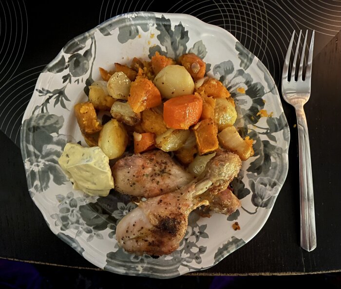 Tallrik med grillade kycklingklubbor, ugnsrostade potatisar, sötpotatis, morötter, palsternacka, lök, butternut och en klick sås.