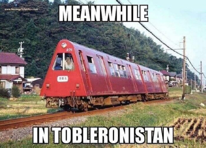 Rött tåg med trekantig front kör på järnvägen; texten "Meanwhile in Tobleronistan" ovanför och under bilden.