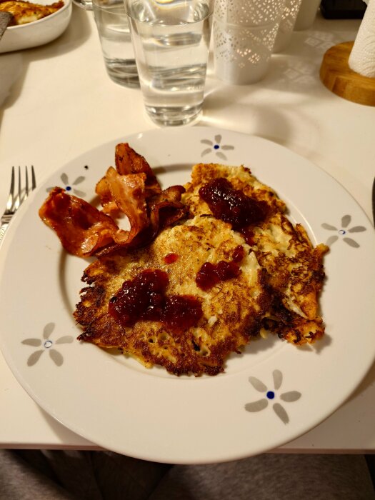 Tallrik med raggmunk och fläsk, serverad med lingonsylt, på ett dukat bord.
