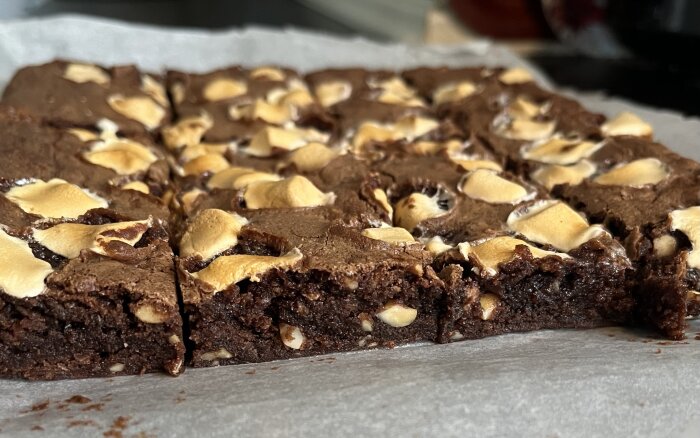 Browniekaka med jordnötter, cashewnötter, hackad choklad och minimarshmallows på bakplåtspapper.