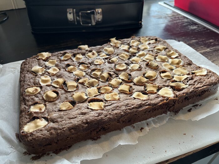 Brownie med jordnötter, cashewnötter, hackad choklad och minimarshmallows på bakplåtspapper, klar att serveras.
