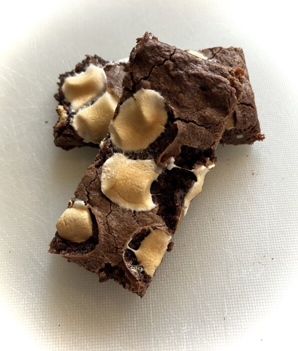 Två brownies med minimarshmallows ovanpå, liggande på en skärbräda.