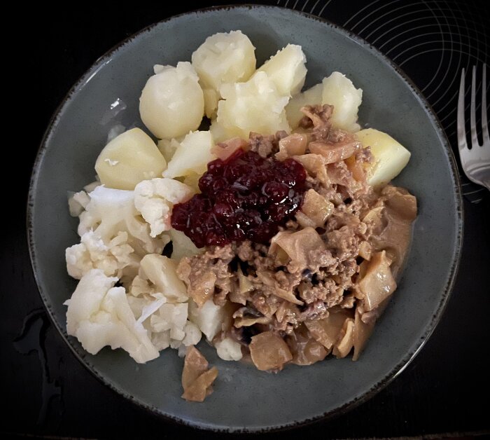 Tallrik med kålpudding, kokt blomkål, kokt potatis och lingonsylt.