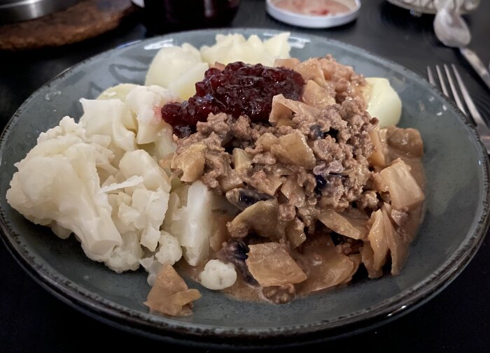 Tallrik med kålpudding, kokt blomkål, kokt potatis och lingonsylt.