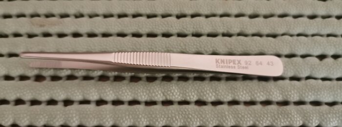 Knipex-pincett av rostfritt stål ligger på en grön, ribbad yta.