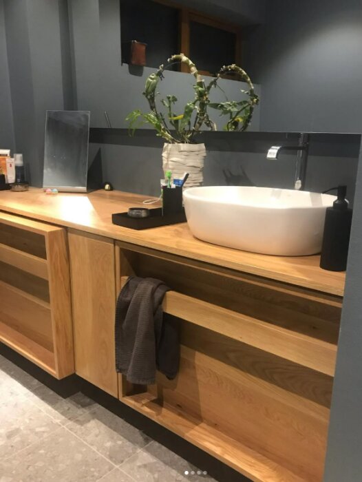 Platsbyggd ekbänkskiva i ett badrum med fristående tvättställ, växt i kruka och diverse badrumsartiklar.