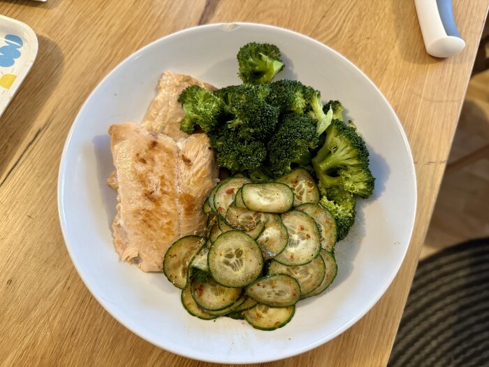 Tallrik med stekt fisk, ångkokt broccoli och skivad gurka med kryddor.