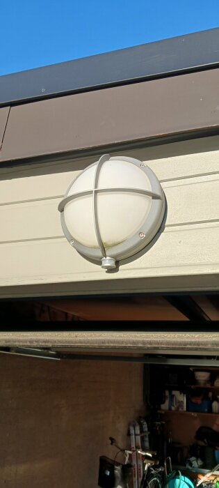 Utomhusvägglampa med skyddsgaller monterad på en garagevägg. Fråga om justering av sensor/känslighet i diskussionsforum.