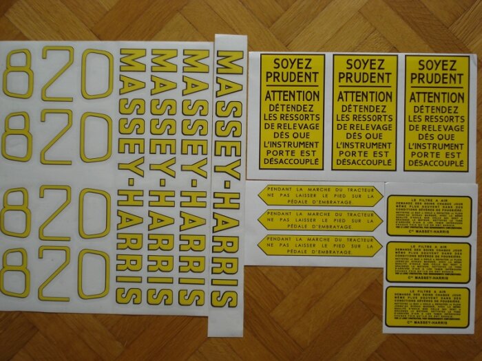 Klistermärken till Massey Harris Pony traktor, gula med svart text, inkluderar varningar och instruktioner på franska, placerade på träyta.