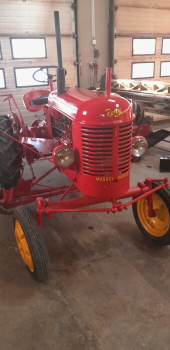 Röd Massey Harris Pony traktor från 1952 i ett garage, med fokus på fronten där text och logga syns.