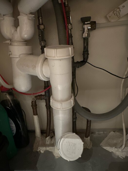 Vattenrör under diskbänk där två kallvattenrör och två varmvattenrör går ihop till ett gemensamt rör, omgivna av avloppsrör och förvaring.