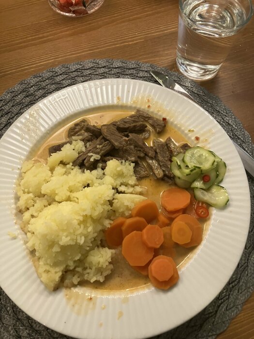Tallrik med långkokt ryggbiff i currysås, pressad potatis, morötter och ingefärsgurka.