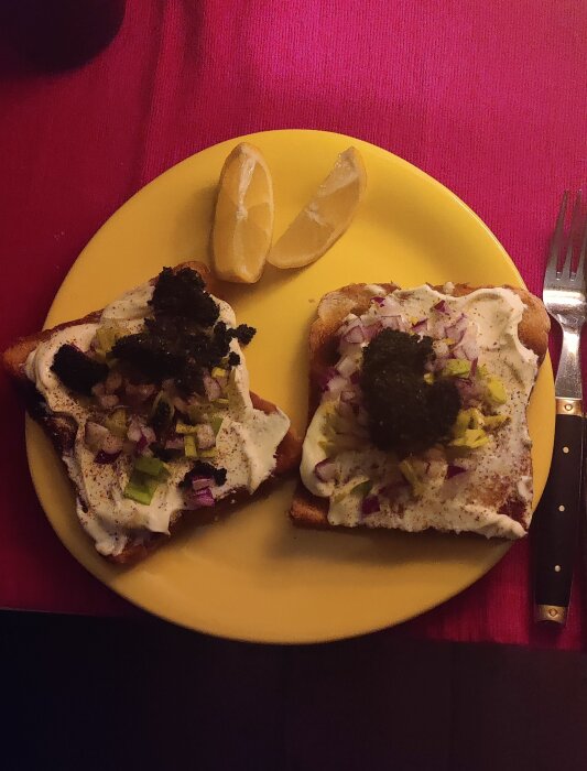 Två smörgåsar med gräddfil, hackad rödlök, grönsakstopping och citronklyftor på en gul tallrik.