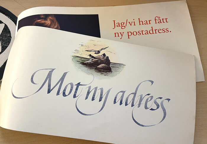 Flyttkort med texten "Mot ny adress" och "Jag/vi har fått ny postadress" i en bok med illustration av fåglar på ett berg.