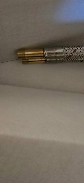 Närbild på två mässingsslangar med kopplingar som ska anslutas till en Tapwell blandare i badrummet, sitter på vit yta.