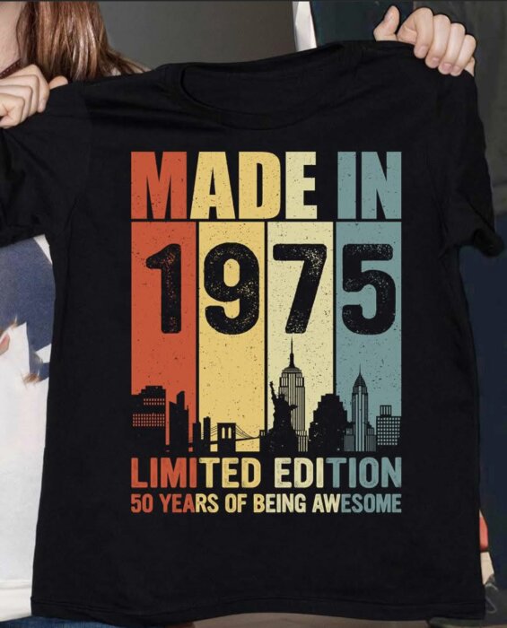 Svart t-shirt med texten "Made in 1975, Limited Edition, 50 Years of Being Awesome" och silhuetter av stadssiluetter i bakgrunden.