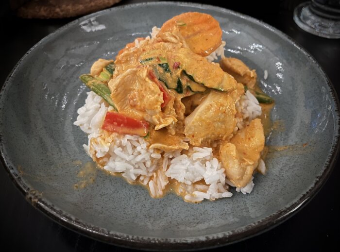 En tallrik med ris och Gaeng Panäng-curry med grönsaker och kyckling i en krämig, röd sås.
