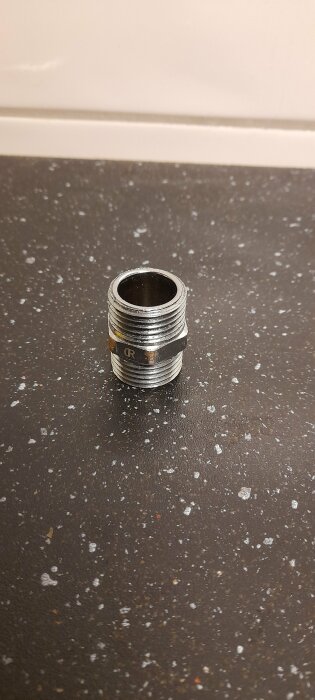 Metallisk gängad rörkoppling på marmorerad yta.