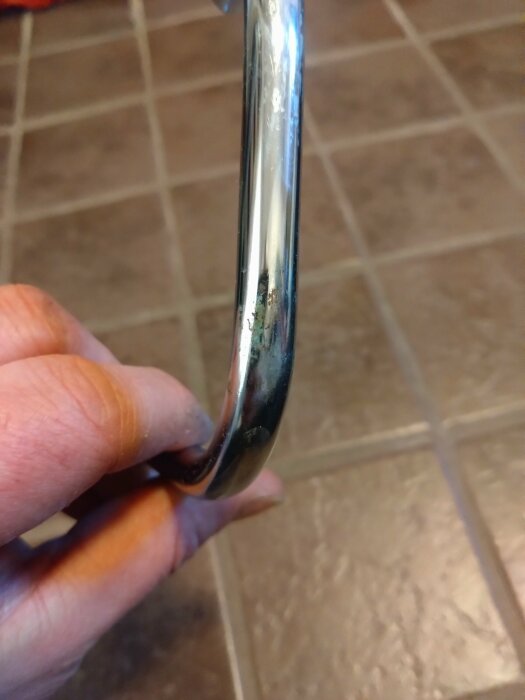 Hand håller i ett kromrör med antydan till en spricka i ett badrum. Röret är en del av en läckande installation.