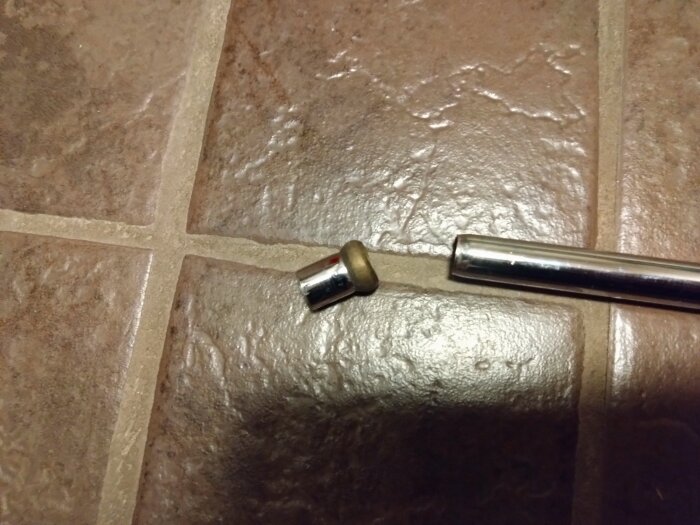 Skadat rör med avbrutna ändar liggande på kakelgolv, visar galvanskt slitage vid konorna.