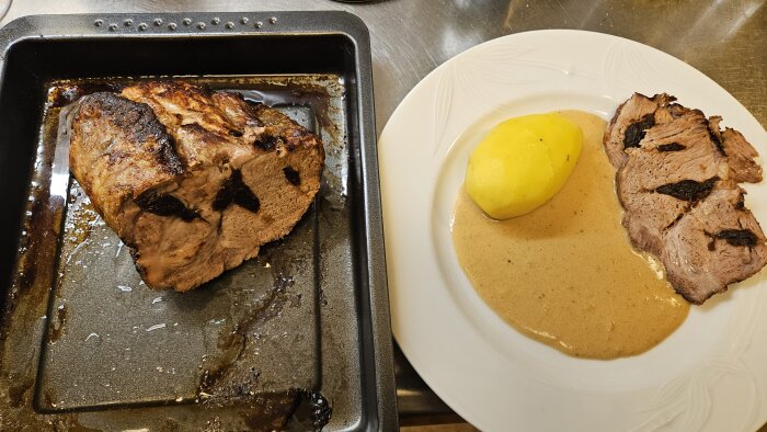 Plommonspäckad fläskkarré i ugnsform bredvid tallrik med skivad karré, gräddsås och kokt potatis.