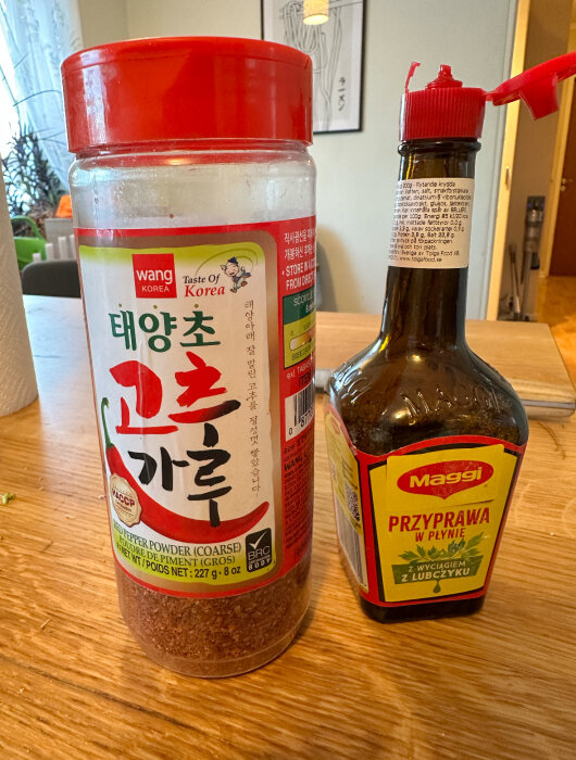 Behållare med koreanskt rödpepparpulver och flaska Maggi kryddsås på träbord.
