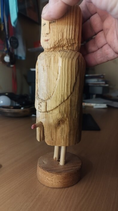 Träfigur i profil med bas och utskjutande del, hålls av en hand.