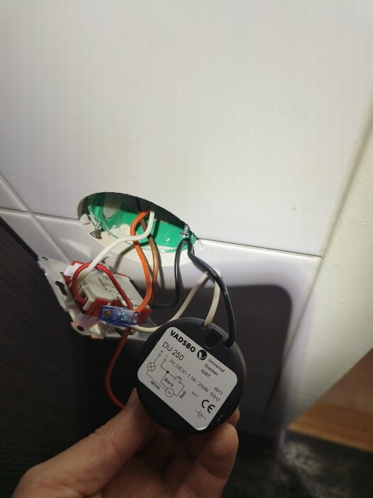 Närbild på en Vadsbo DU-250 dimmer med anslutna elkablar i ett installationsutrymme bakom en väggplatta.