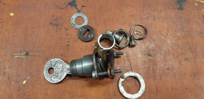 Trasigt tändningslås på träbord, visar cylinder, nyckel med symbol och muttrar, letar information om symbolen, passar ej i panelens hål.