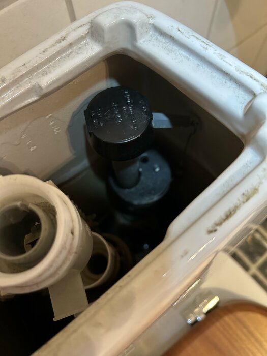Närbild av en toalettcisterntank med inloppsrör, synlig flottör och plastkomponenter, undersökning av möjlig läcka och demontering.