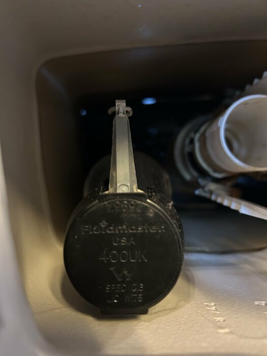 Närbild av en toalettcisterndel märkt "Fluidmaster USA 400UK". Deluxe från ovansidan, med inloppsrör och flottör.