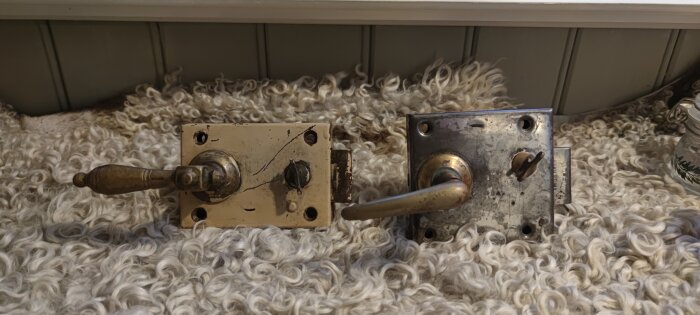 Två kammarlås på en yllefilt, det vänstra med en dekorativt formad knopp och det högra med en enklare rak knopp.