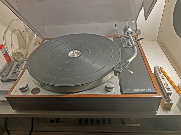 Skivspelare Thorens 150 med SME 3009 tonarm på ett bord, delvis täckt med plastlock, omgiven av olika objekt.