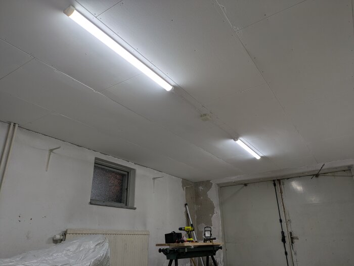 Ceiling with new lighting fixtures in a renovated room, walls partially unfinished, showing construction tools and materials.