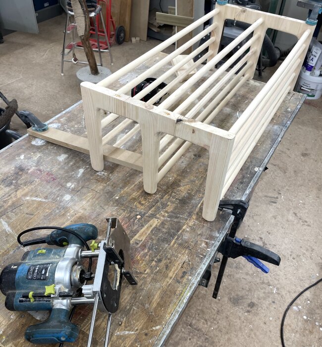 Träkonstruktion för en hylla på ett arbetsbord, bredvid en överhandsfräs med trälåsning, i en snickarverkstad.