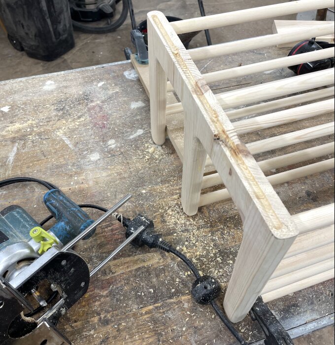 Trähylla under konstruktion på en arbetsbänk, omgivet av verktyg och träspån.