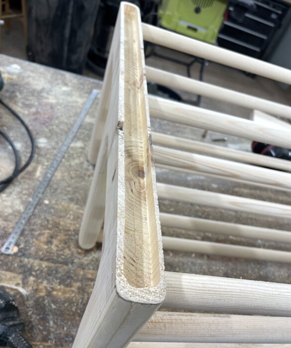 Öppen trästruktur påbörjad för skohylla, med frästa spår längs en sida, omgiven av verktyg och arbetsbänk i snickarverkstad.