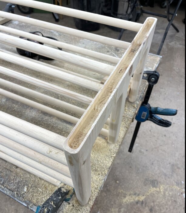 Trähylla under arbete, tvingad på arbetsbänk, visar fräst spår för ekkonsoler. Verktyg och sågspån synliga runtom.