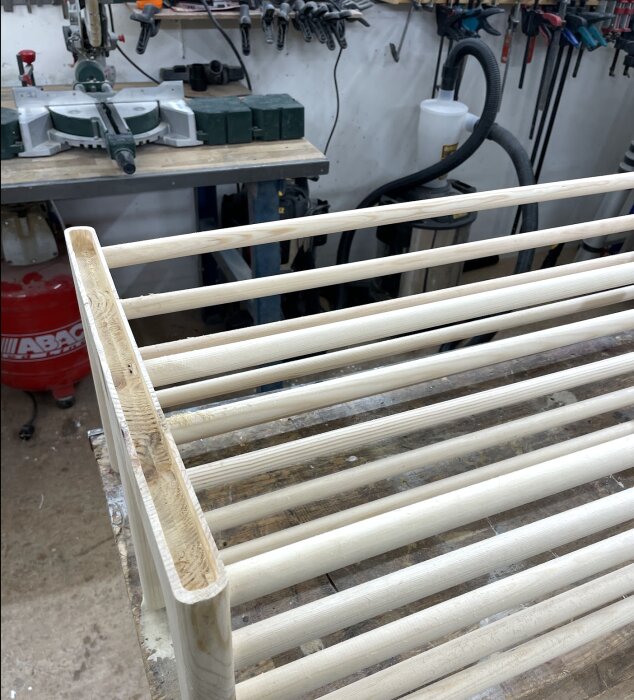 Trähylla under konstruktion i ett snickeriverkstad, visar frästa kanter och rundade hörn. Bakgrunden har verktyg och utrustning.