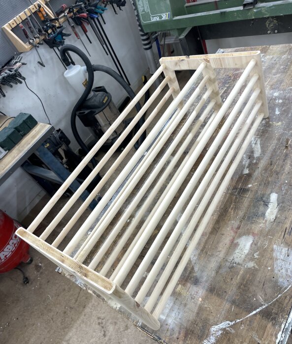 Trähylla under konstruktion i snickarverkstad, placerad på ett arbetsbord med verktyg i bakgrunden.