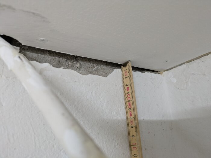 A measuring stick is placed in a gap between a ceiling and wall corner showing uneven alignment.