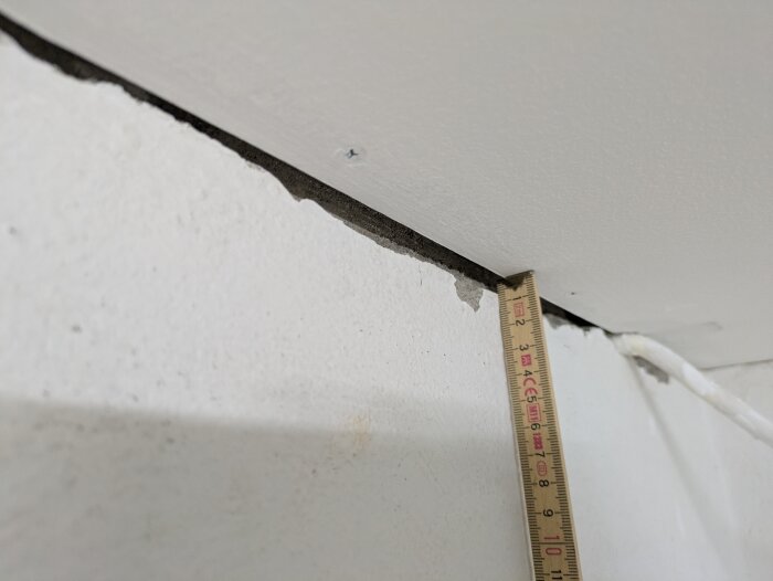 Gap between wall and ceiling with a ruler for measurement, suggesting challenges in applying caulking accurately.