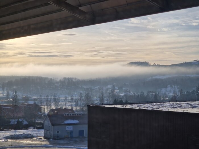 Utsikt från ett sjukhus i Torsby visar dimma över skog och hus i ett vinterlandskap under en gråmulen himmel.