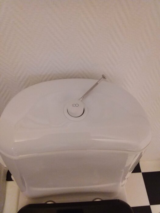 En skruvmejsel nära tryckknappen på en toalettcistern.