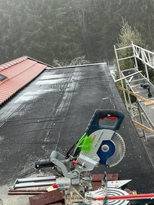 Takkupa med ytpapp och synliga "släppor", cirkelsåg i förgrunden, byggställning och skog i bakgrunden.