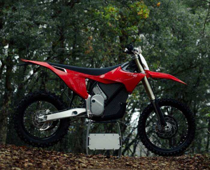 Röd och svart elektrisk motorcykel i skogsmiljö, liknande Honda, på ett ställ.