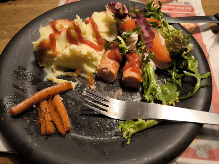 Tallrik med grillkorv, potatismos, sallad och smörstekta morötter.