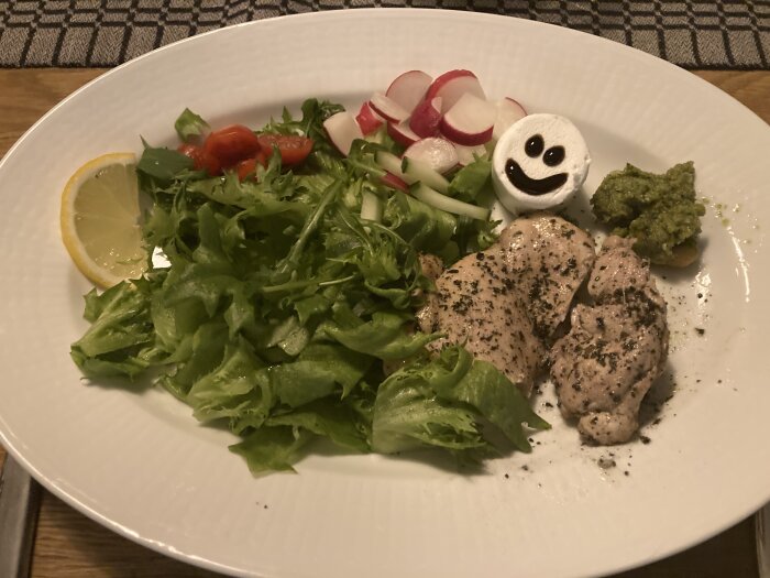 Kycklinglår med salsa verde, sallad, rädisor, tomater, citron och Chevreost med glad ansikte av crema de balsamico på tallrik.