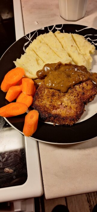 Tallrik med schnitzel av julskinka, brun sås, potatismos och morötter.